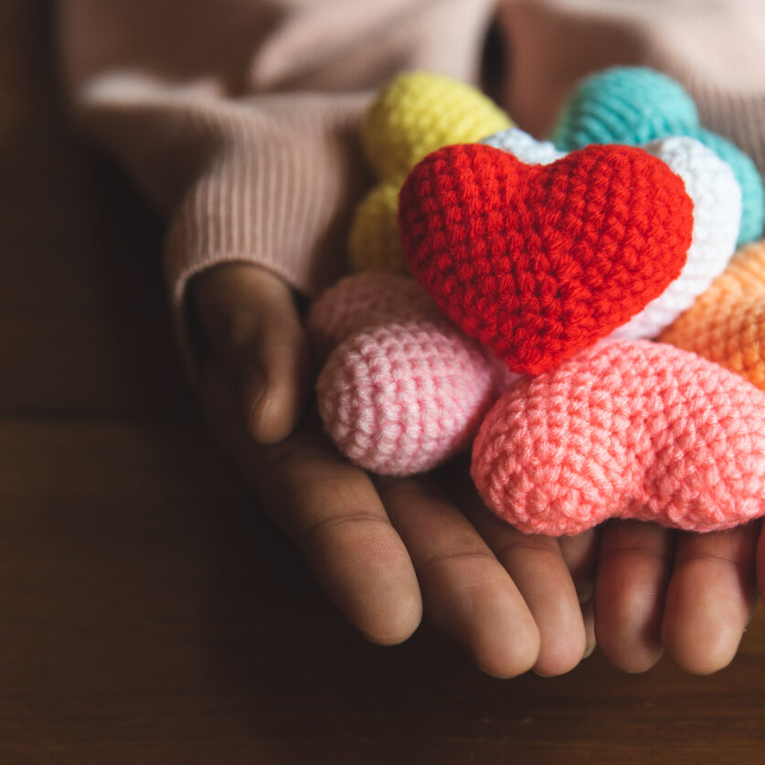 Mixed colors yarn heart on giving hands. Close up of colorful handmade. Heart donation concept. Valentine  love forever theme Mixed colors yarn heart on giving hands. Close up of colorful handmade. Heart donation concept. Valentine  love forever theme