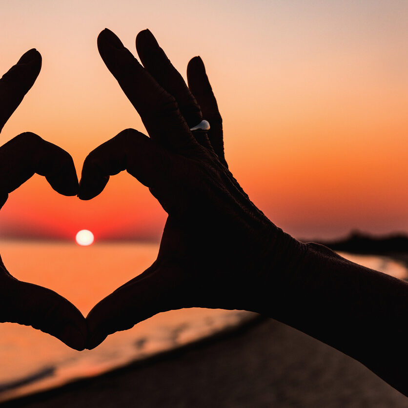 Close up of heart made by female hands background the sunset sea. Vintage effect style pictures. Close up of heart made by female hands with rings background the sunset sea. Vintage effect style pictures. Love concept.